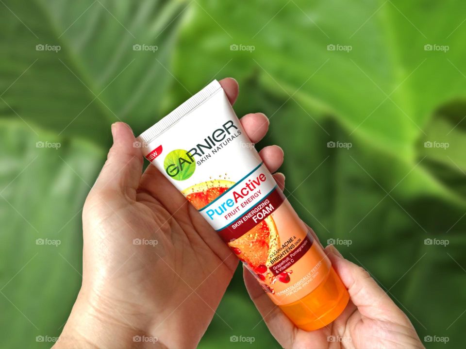 Hand holding a tube of beauty product, a cleanser for acne prone skin against green background 