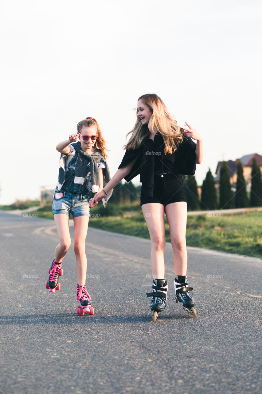 Teenage smiling happy girls having fun rollerskating together on summer day