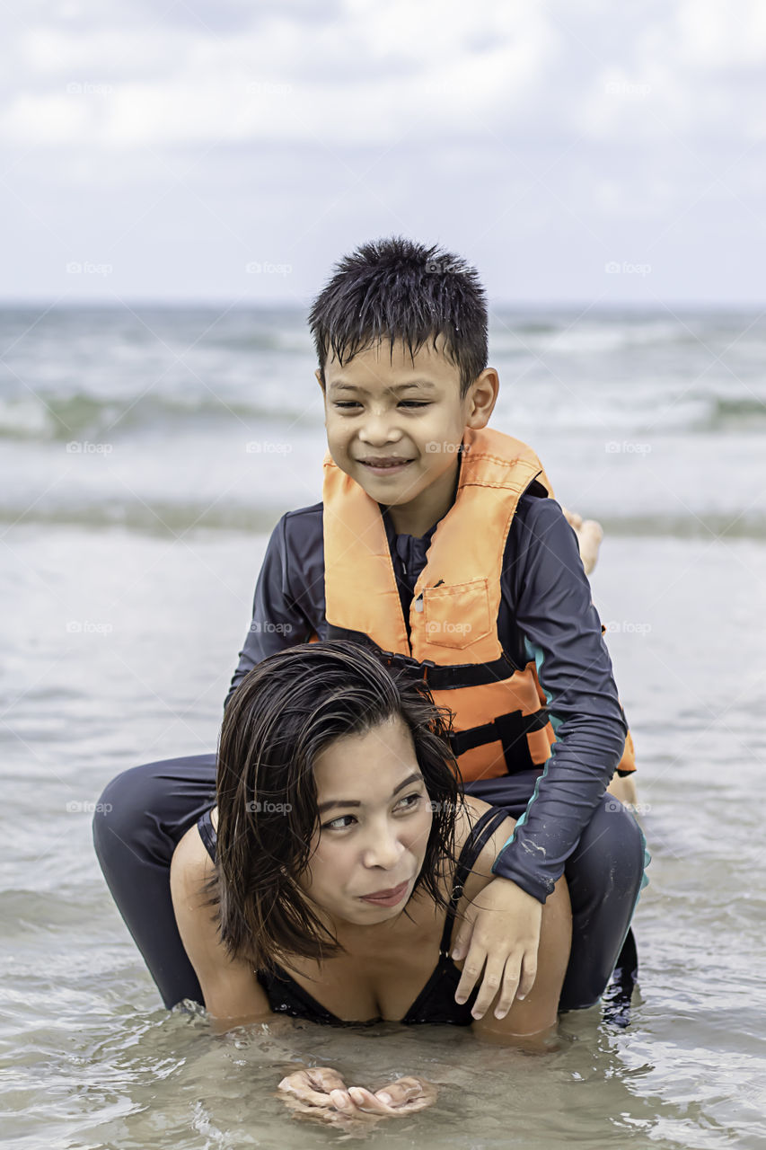 Asian boy sitting on the back of a woman playing in the sea.