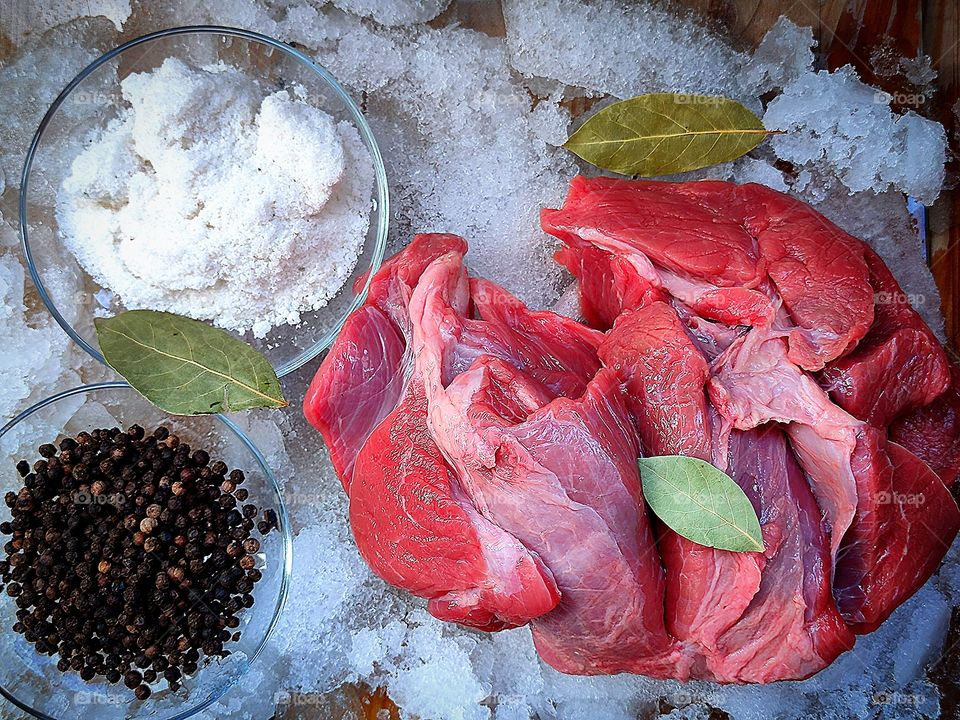 there is a fresh piece of meat on the ice, a saucer of black peppercorns, a saucer of white salt and a few leaves of bay leaves