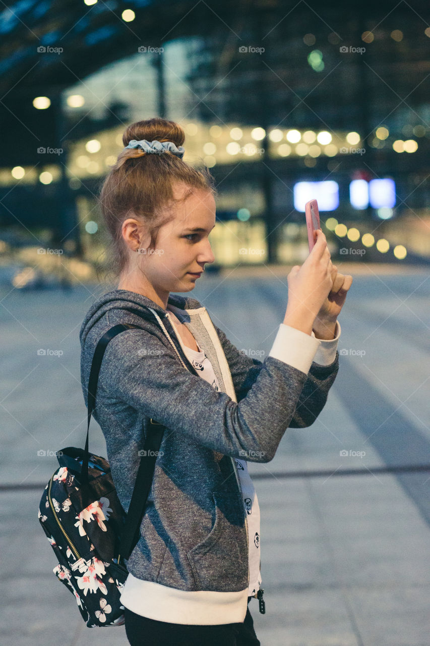 Young woman looking at screen of smartphone during walk in the city at night