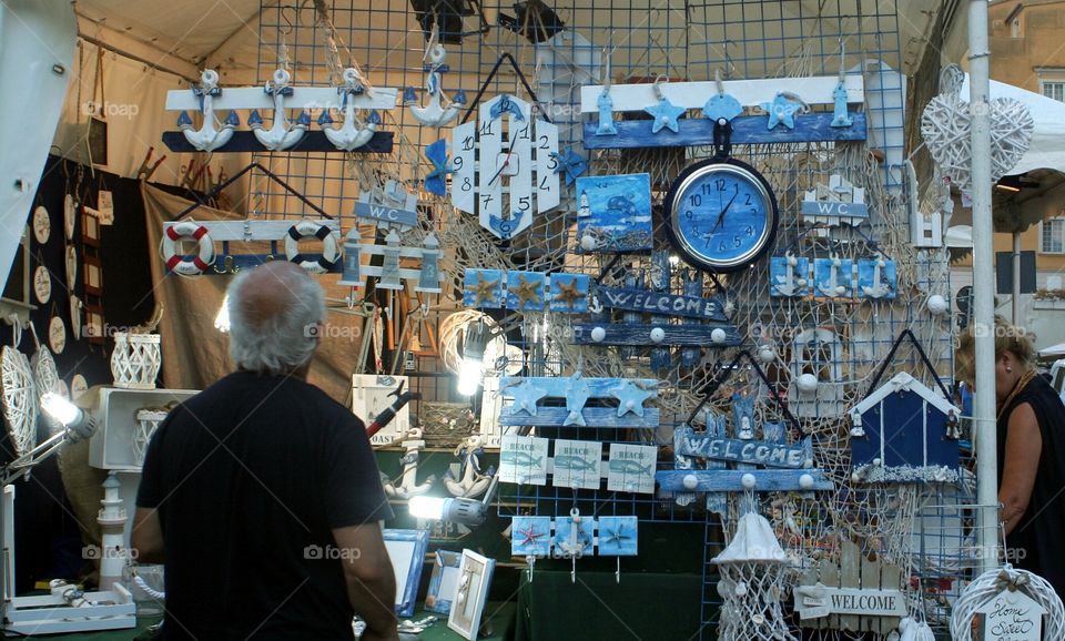 Old man observes souvenirs for selling in a street shop.
