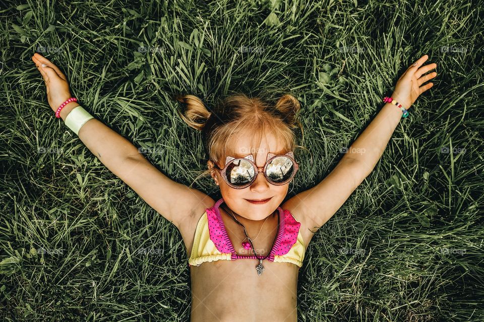 relaxed little girl lies on a green lawn in a swimsuit