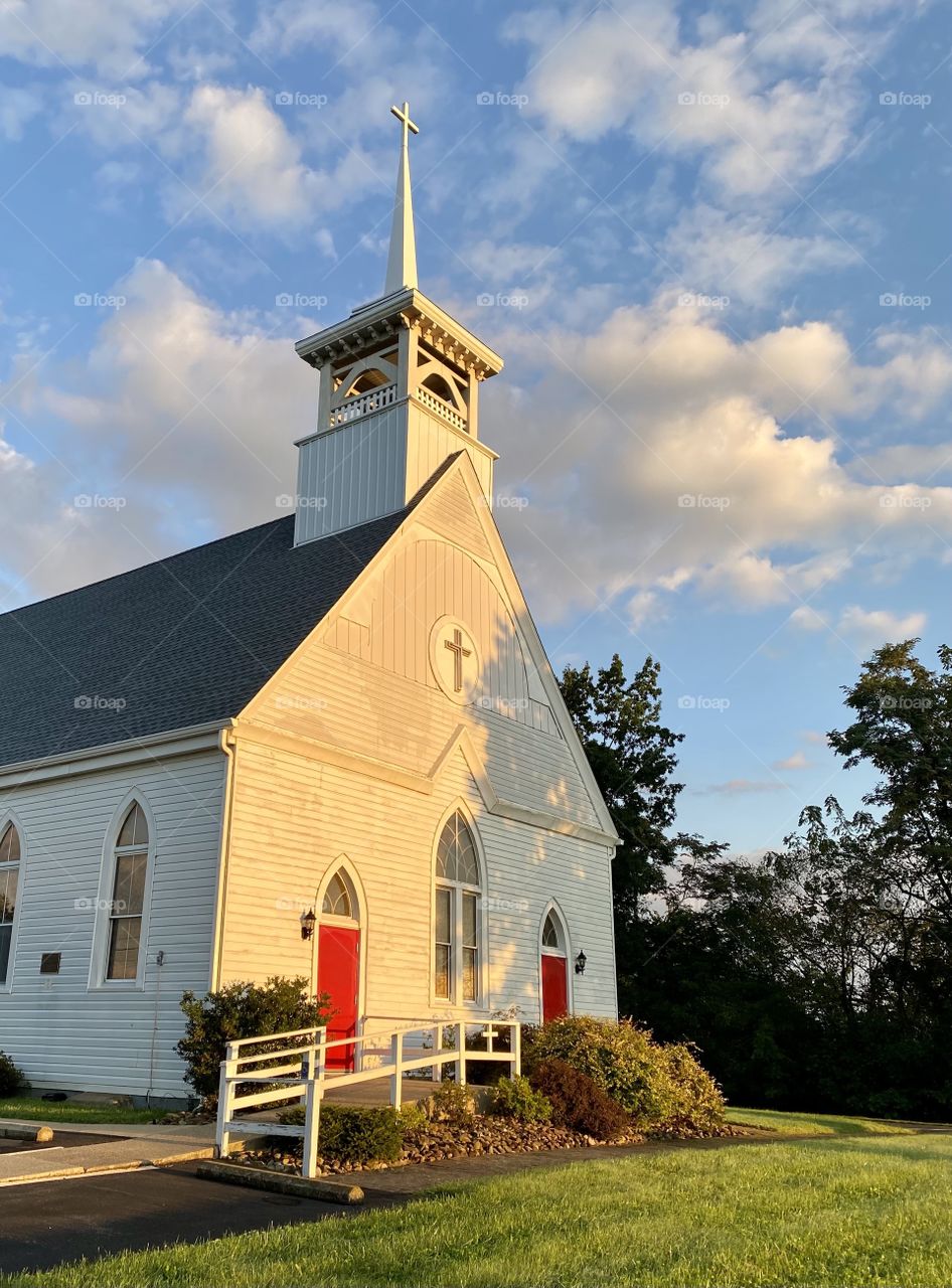 Early morning sun shining on a white church with red doors