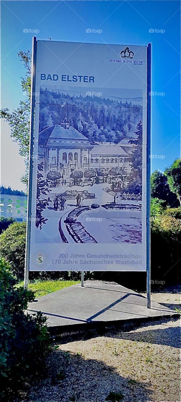 The large sign adorned with a historical print of the town of „Bad Elster“ featuring the town’s well known sights. Located in the „Lüneburger Heide“, a large flat land area in „Saxony“ or „Sachsen“, Germany. 2022. Hypnotic Productions