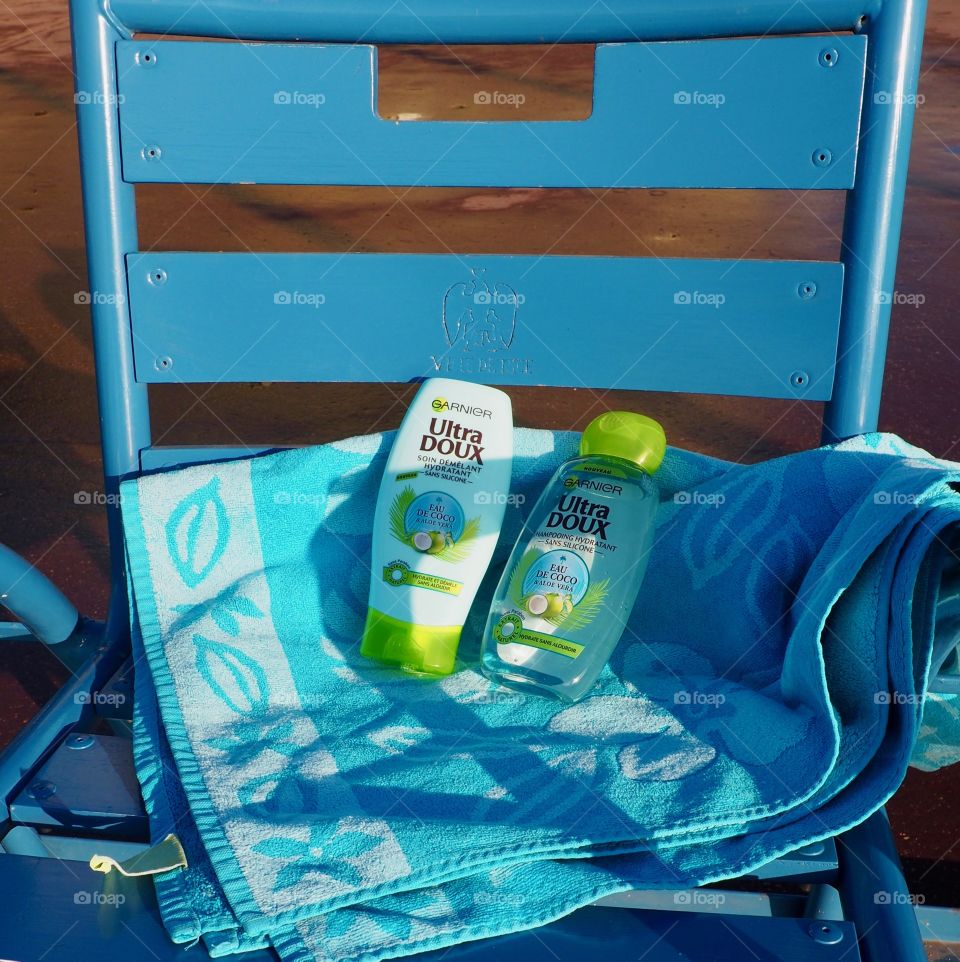 Garnier eau de coco shampoo and conditioner on blue beach towel and blue chair in Nice, France.