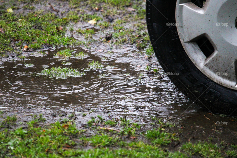 A cars wheel near a rain puddle on the ground