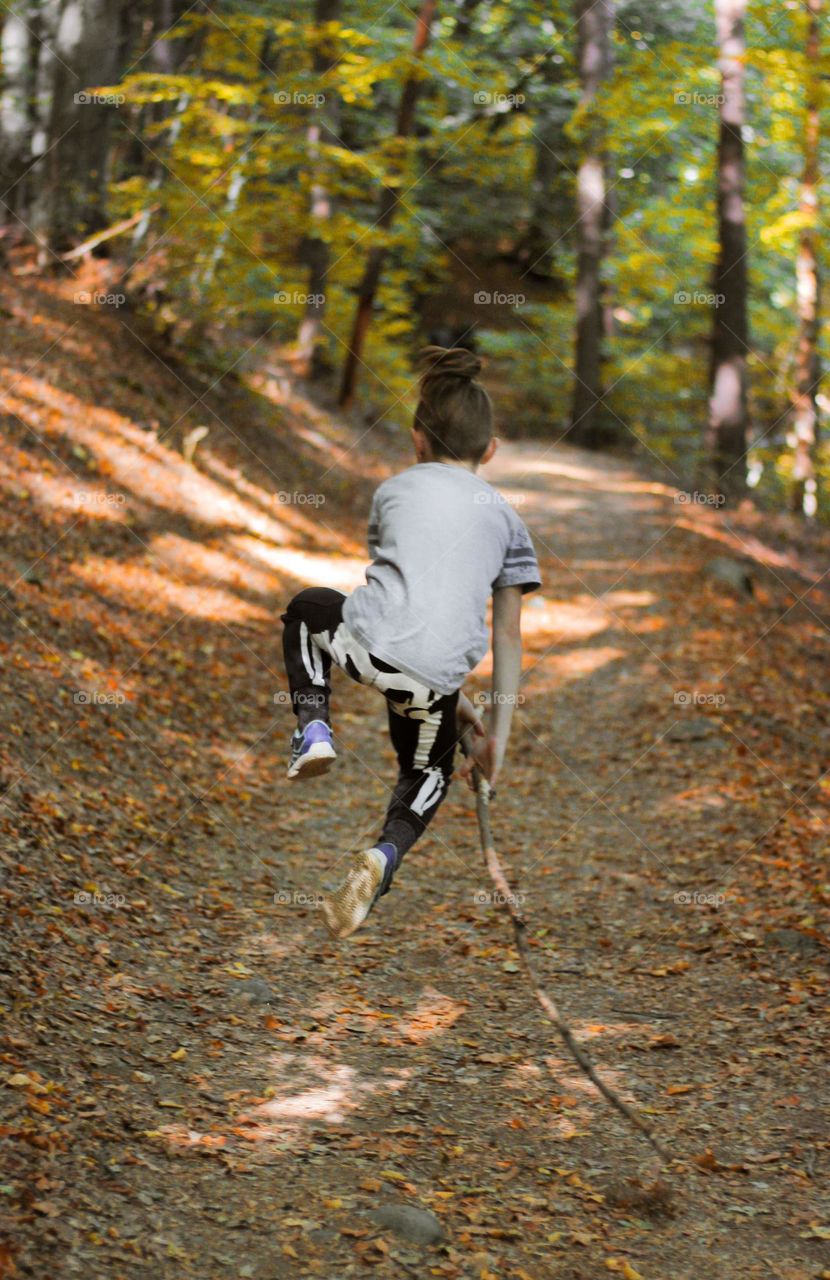 A boy jumping at the footpath of fallen autumn leaves