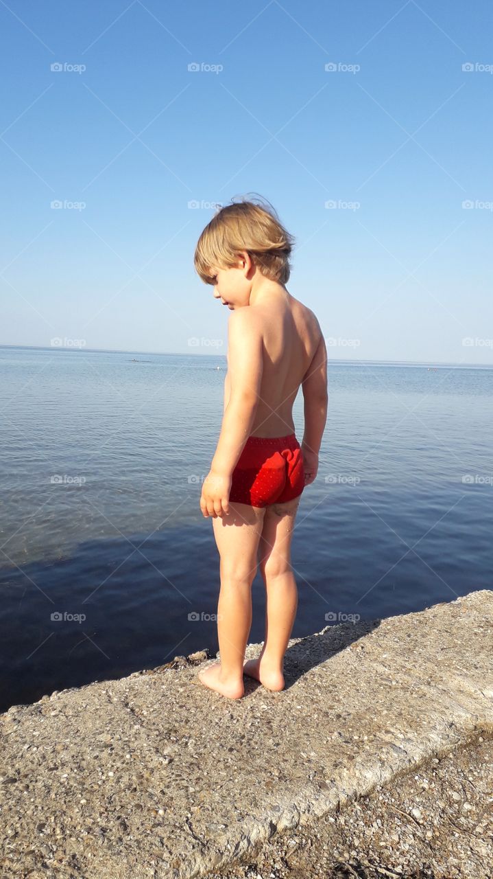 little boy stands on the shore and looks at the water