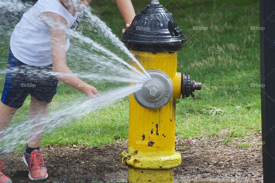A boy in a New York City  park cooling off from the water flowing out of an open fire hydrant.