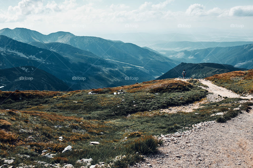 Young man with backpack hiking in a mountains, actively spending summer vacation. Tatra Mountains landscape. Scenic view of mountain rocky peaks, slopes, hills and valleys covered with grass, mugo pine and trees