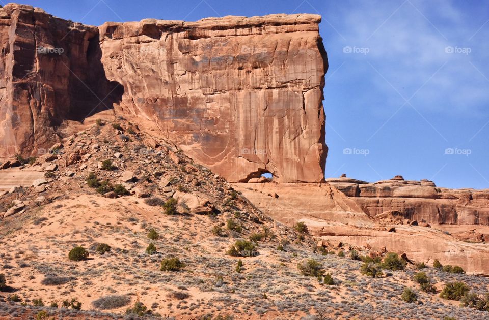 A sunny day in Moab with a beautiful geological feature with scrub brush and clouds.