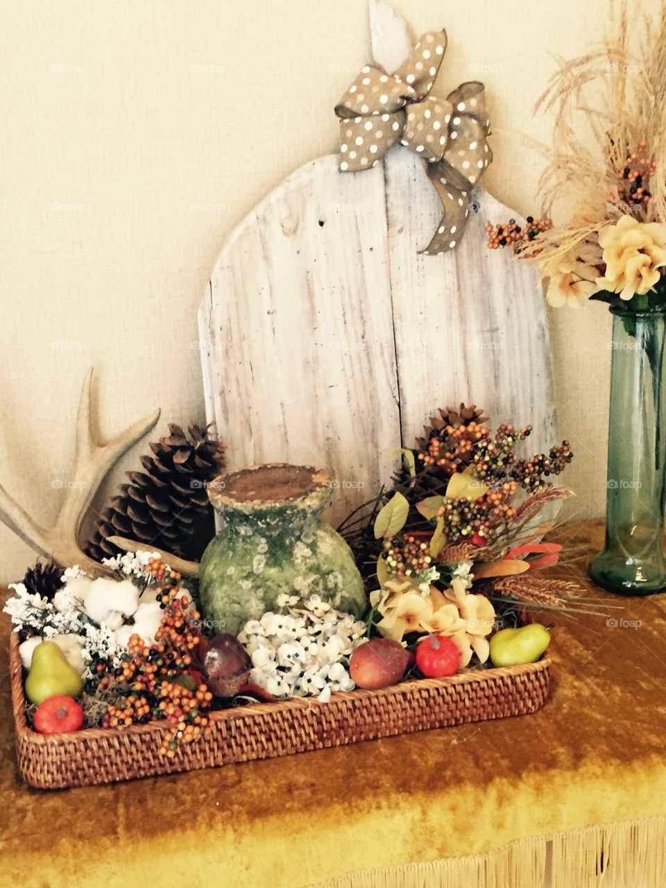 Fall decorations including, fall flowers, large pine cones, teeny pumpkins, making a gorgeous display in an oblong wicker basket. 