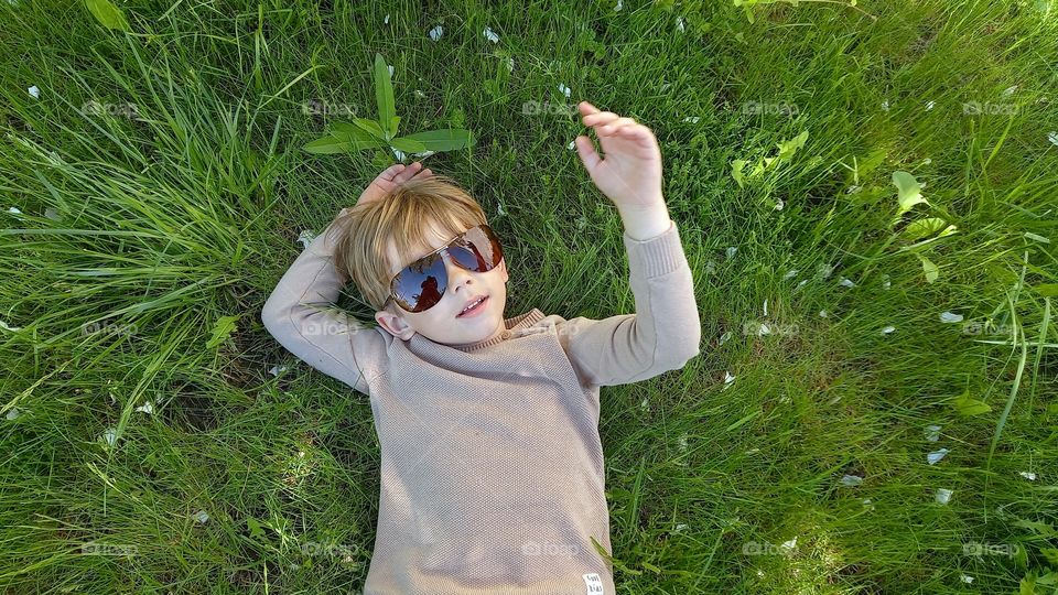 little boy wearing sunglasses is lying on the grass