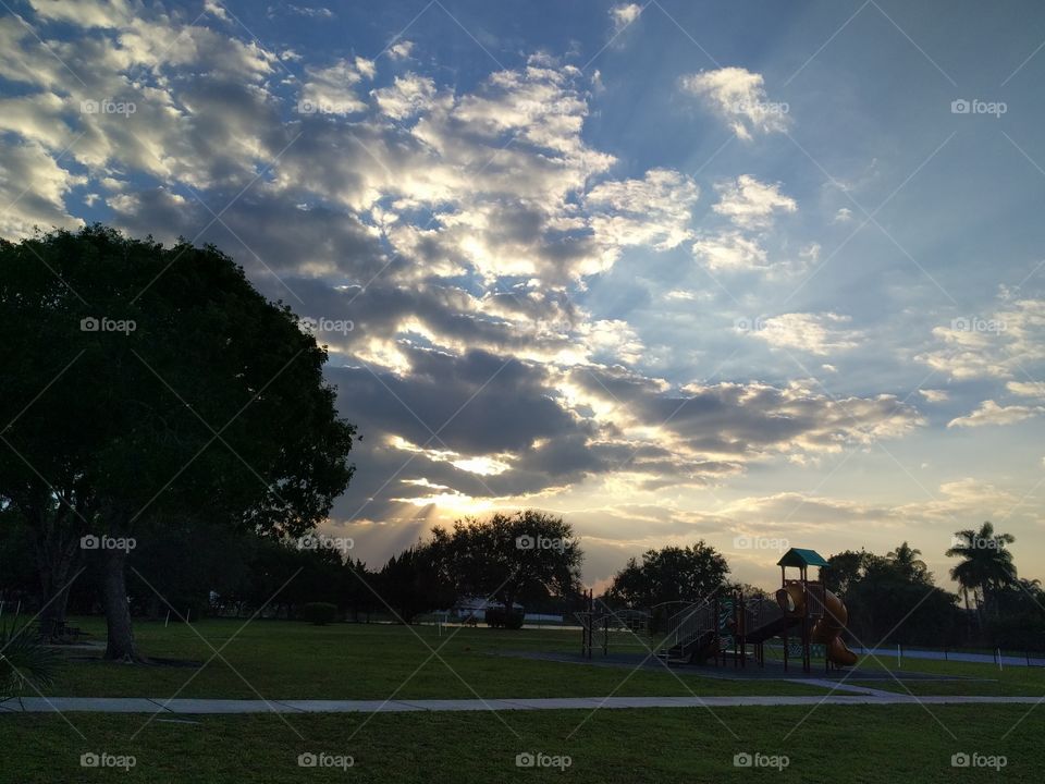 Sun rays showing through white and gray clouds in a blue sky