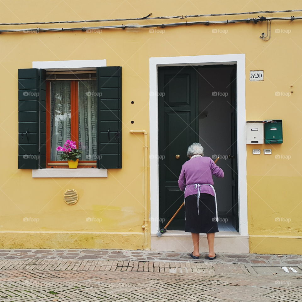 colorful life in Burano. old lady cleans her house in Burano, Italy