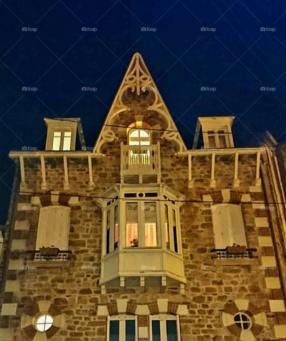 Illuminated windows of the facade of a typical Breton house in bricks, stones and wood at nightfall in Port-Louis under a navy blue sky