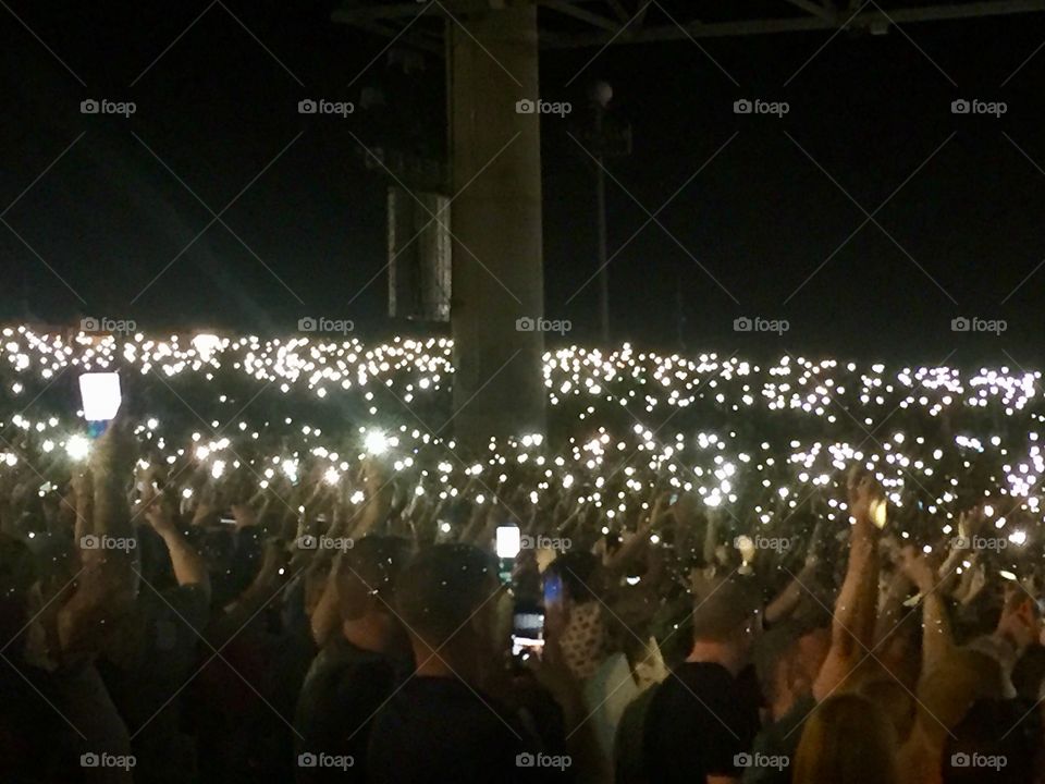 Phone screens lit up at night in the audience at a concert.