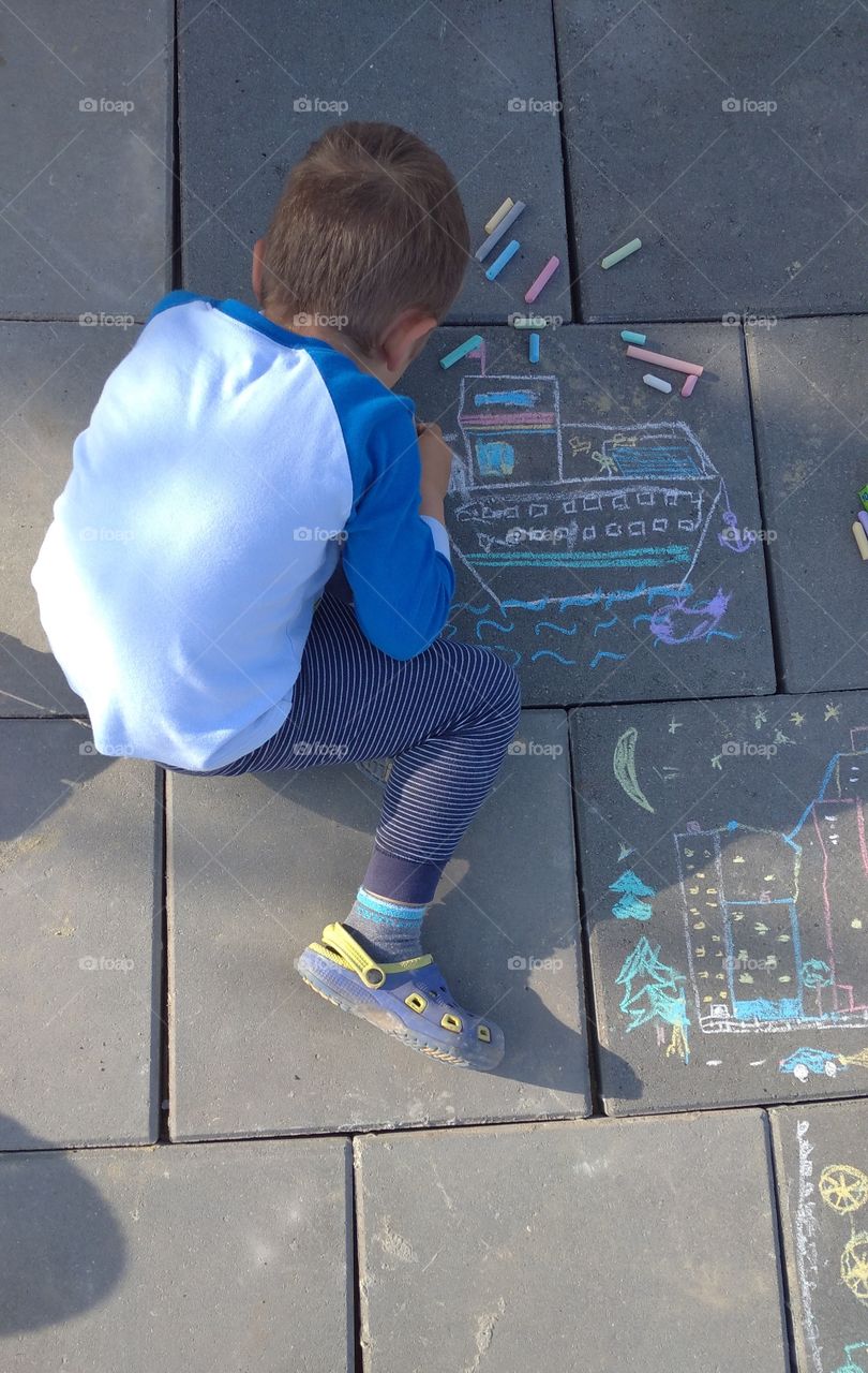 A kid drawing on the street. Chalk drawings on the street pavement.