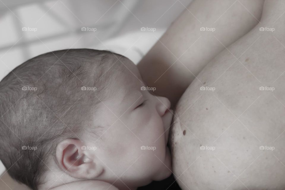 Baby sleeps while suckling on his mother's breast.