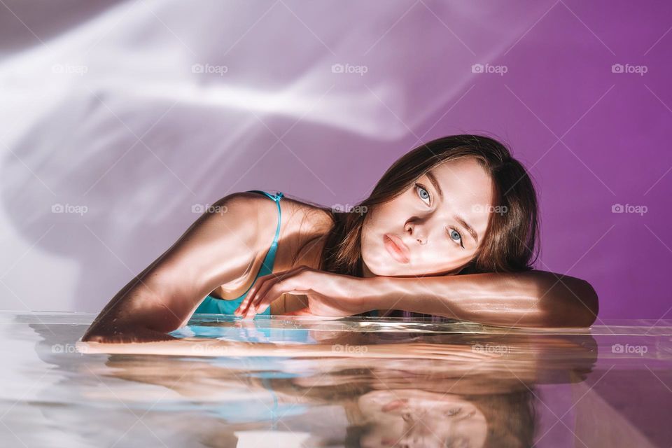 Beauty portrait with water of young woman fashion model with healthy dark long hair on purple background