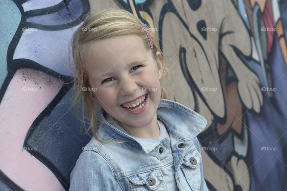 Happy smiling girl in a denim jacked with graffiti wall