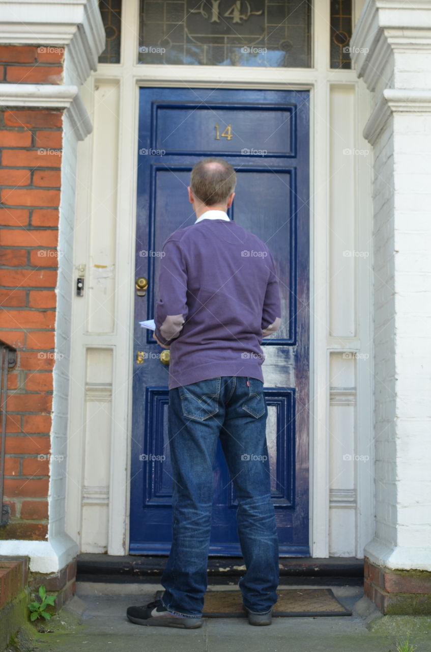 Male canvasser knocking on a blue door and standing outside