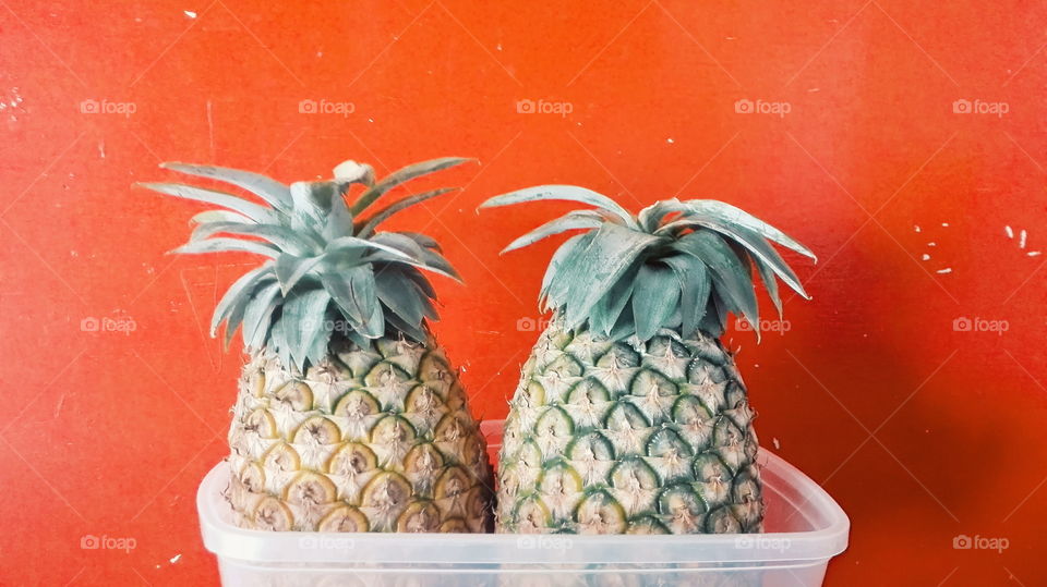 Two pineapples against orange wall