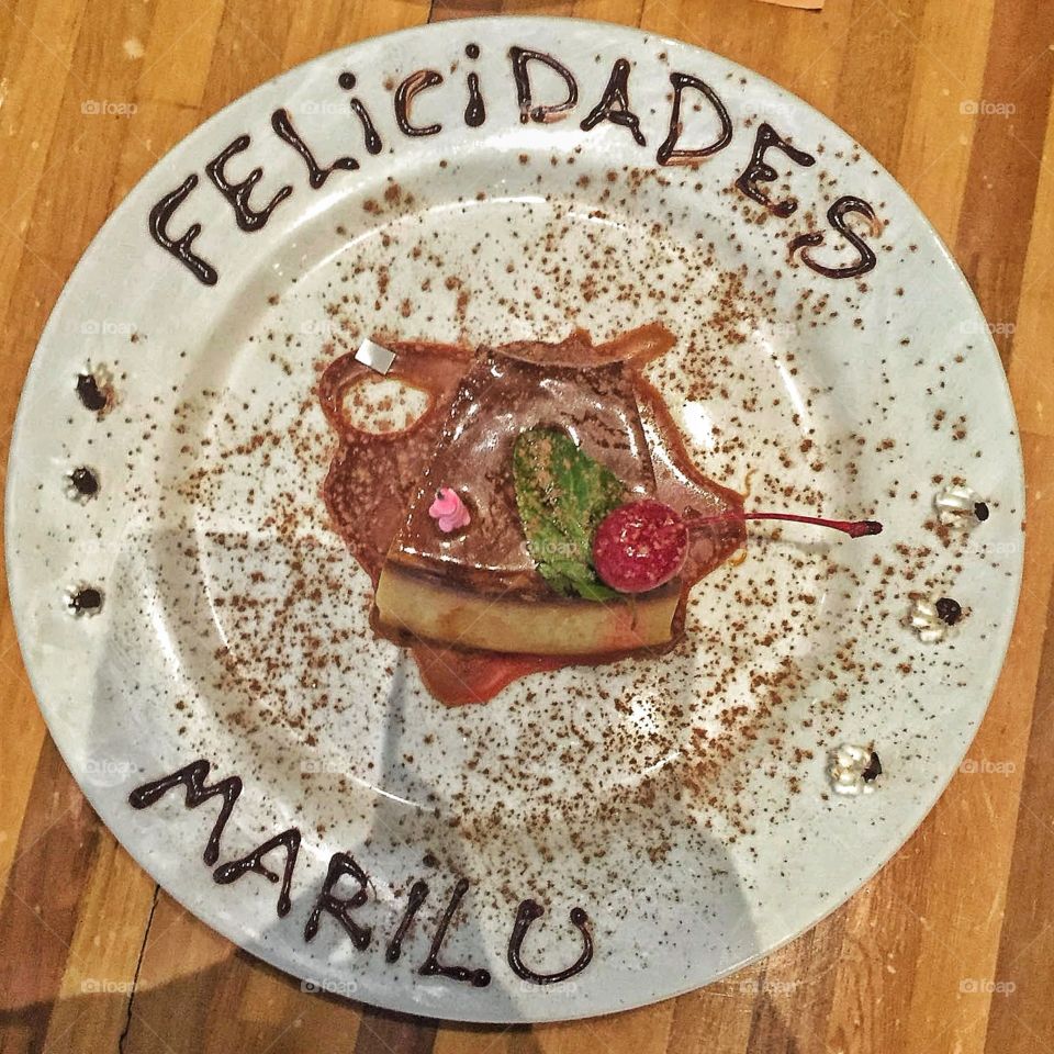 A vanilla and chocolate desert sprinkled with cinnamon, "felicidades Marilu" is written on the dish.