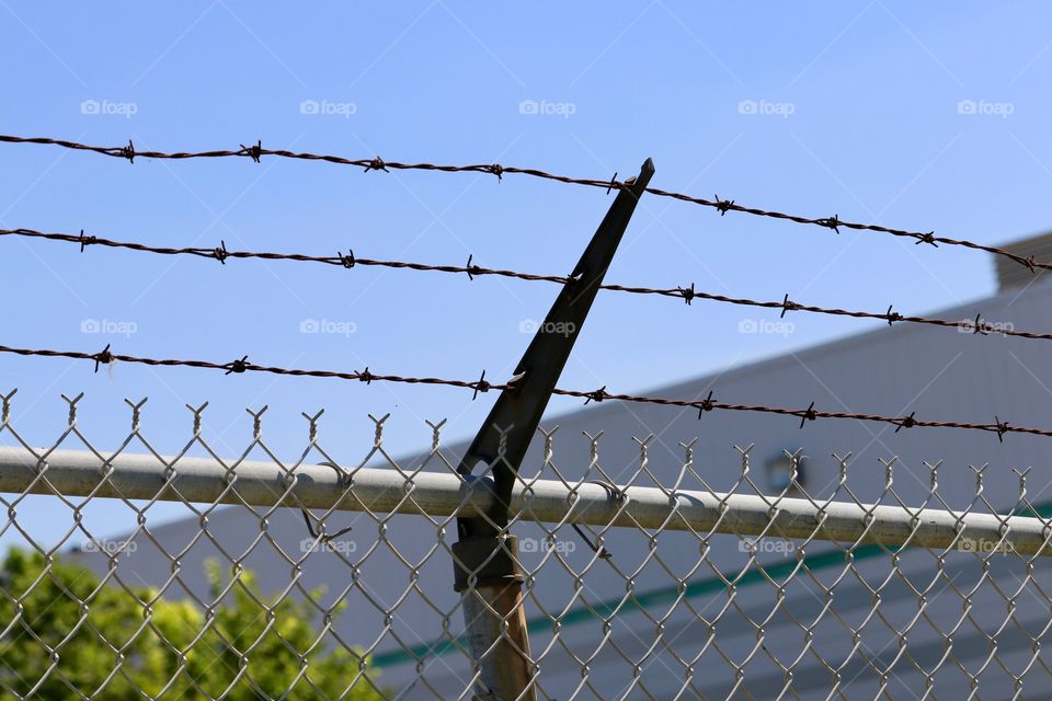 Three strings of barbed wire atop chainlink fence outdoors 