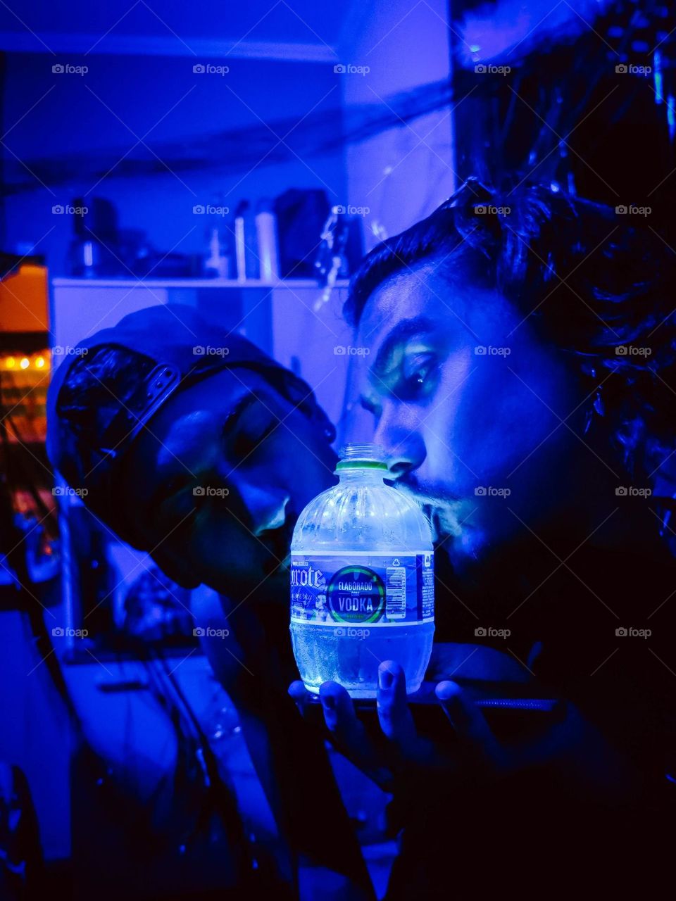 Two men kissing a glowing bottle of cachaça, beautiful close up portrait of a Corote Bottle Purple and blue colors on the photography.
Dois homens beijando uma garrafa de Cachaça Corote