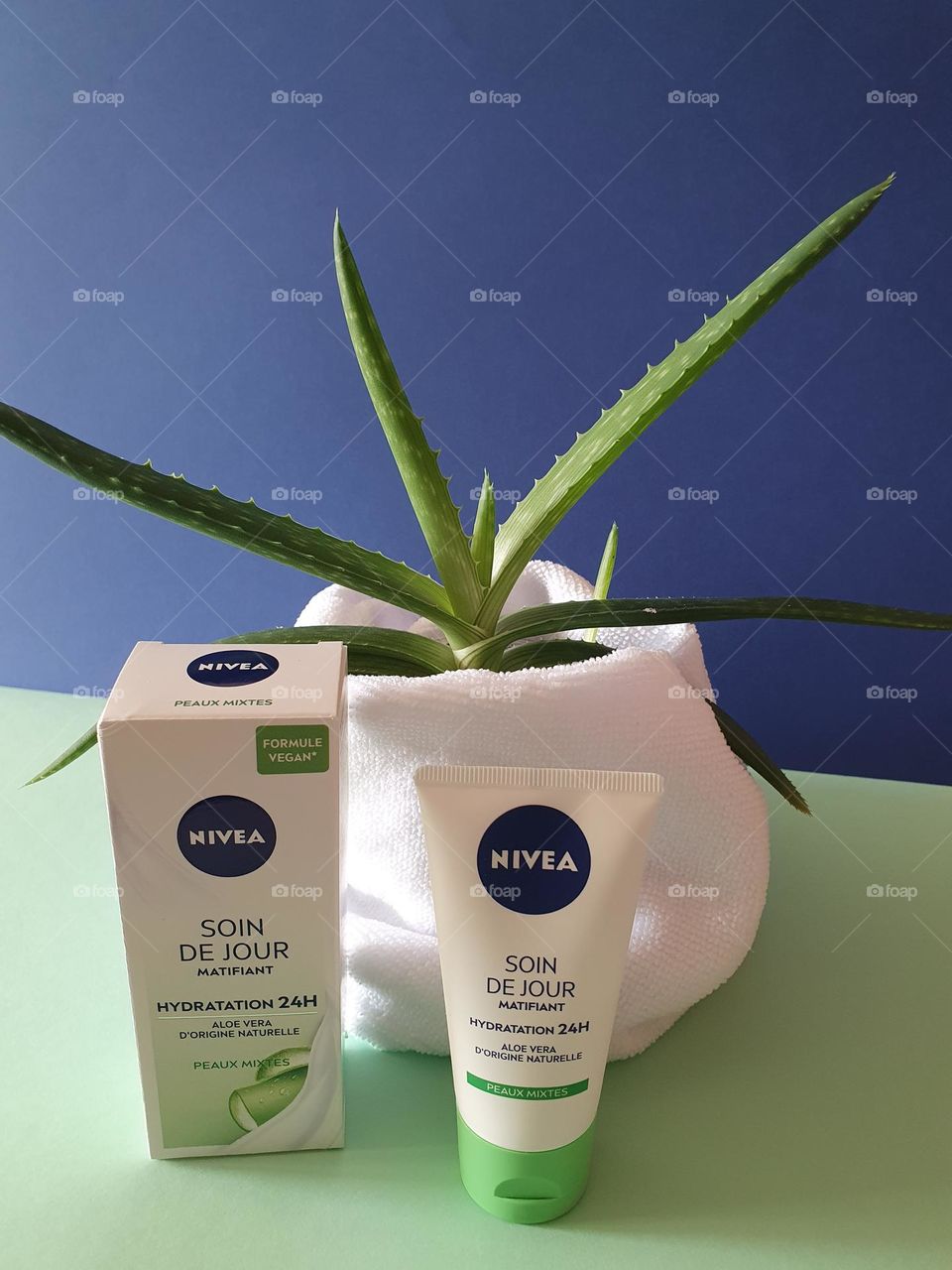 Box and tube of Nivea day moisturiser, 24h moisture - combination skins - mattifying day care - vegan formula - natural origin aloe vera, presented on a green paper surface with a navy blue background in front of an aloe vera and a white towel