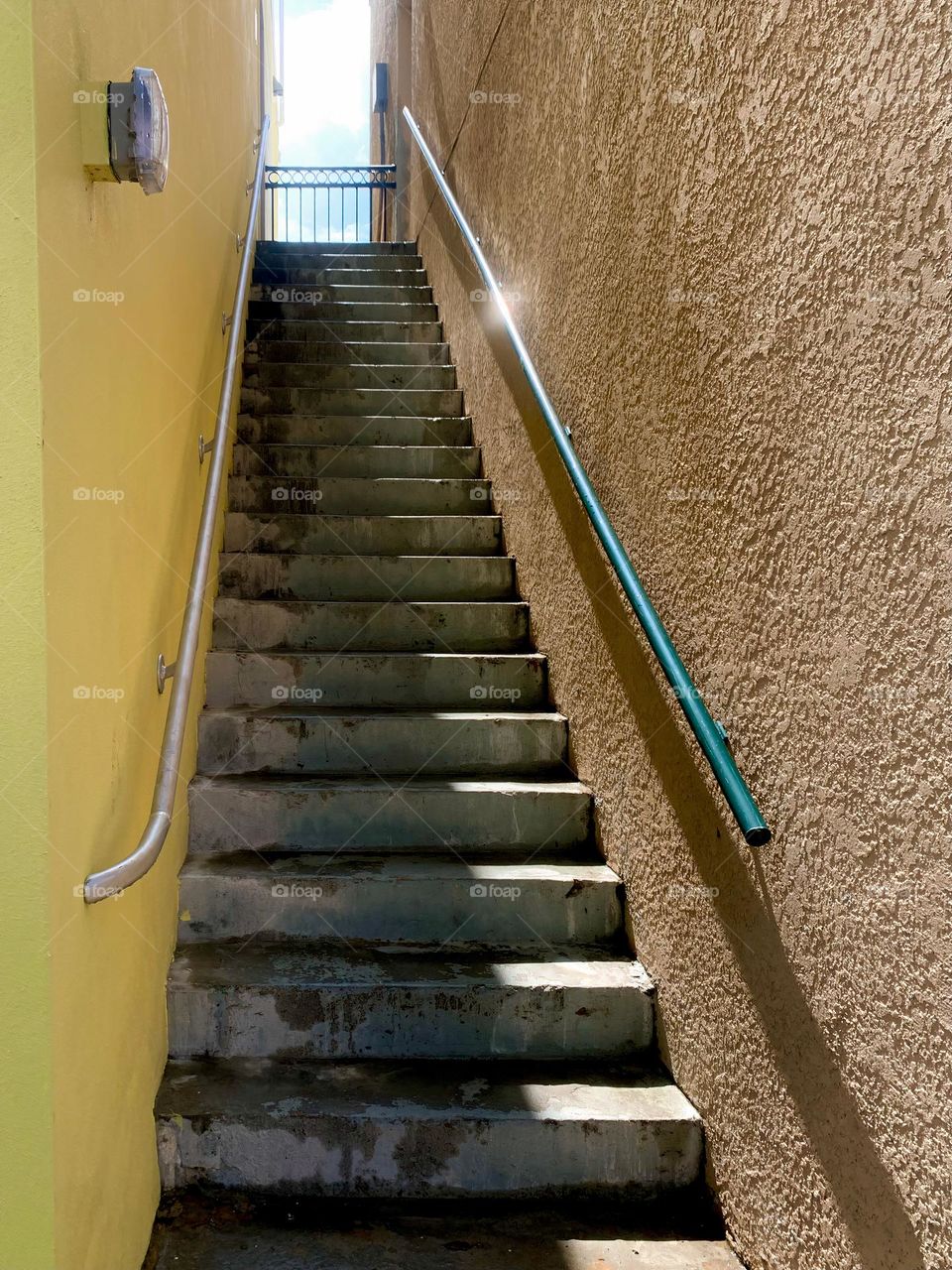 Historic part of the city central eastern Florida at the end of the day with sunlight lighting down stage stairs from above the stairway outside behind the gate creating shadow effects on stucco yellow and orange wall close-up.