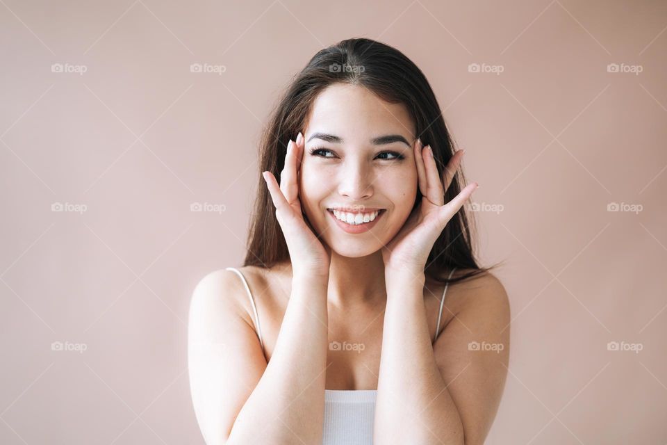 Beauty portrait of young asian woman with healthy dark long hair in top on beige background