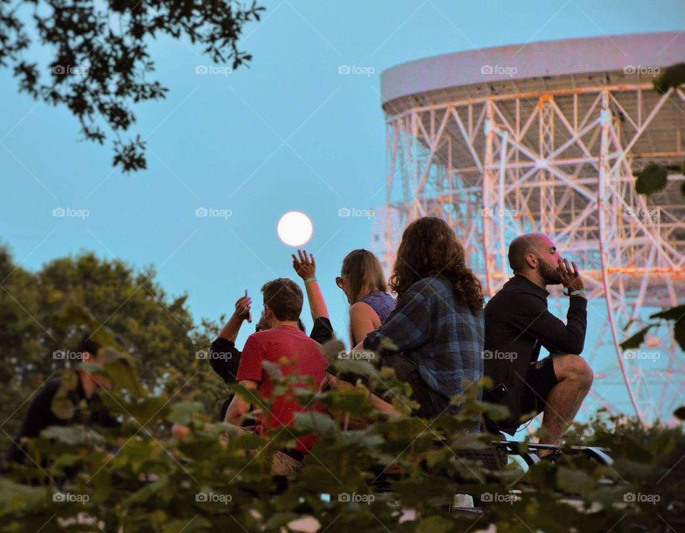 Festival Goers sat on top of a 4x4 Vehicle listening to Music, smoking and raising their hands in the Air, Celebrating the Moonrise next to the Lovell RadioTelescope, at the Blue dot Festival held at Jordrell Bank in Cheshire in the UK.