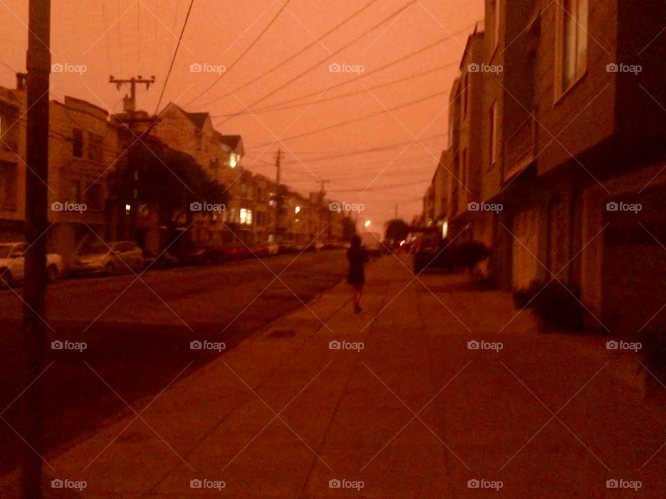 Woman hurrying to go home under an apocalyptic orange sky on 9/9/2020 in San Francisco, California caused by the smoke coming from major wildfires throughout the region