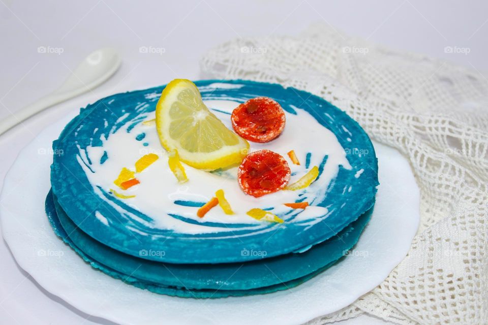 Blue pancakes with sour cream and candied fruit on a white plate.  Excellent breakfast.  Angle view of food