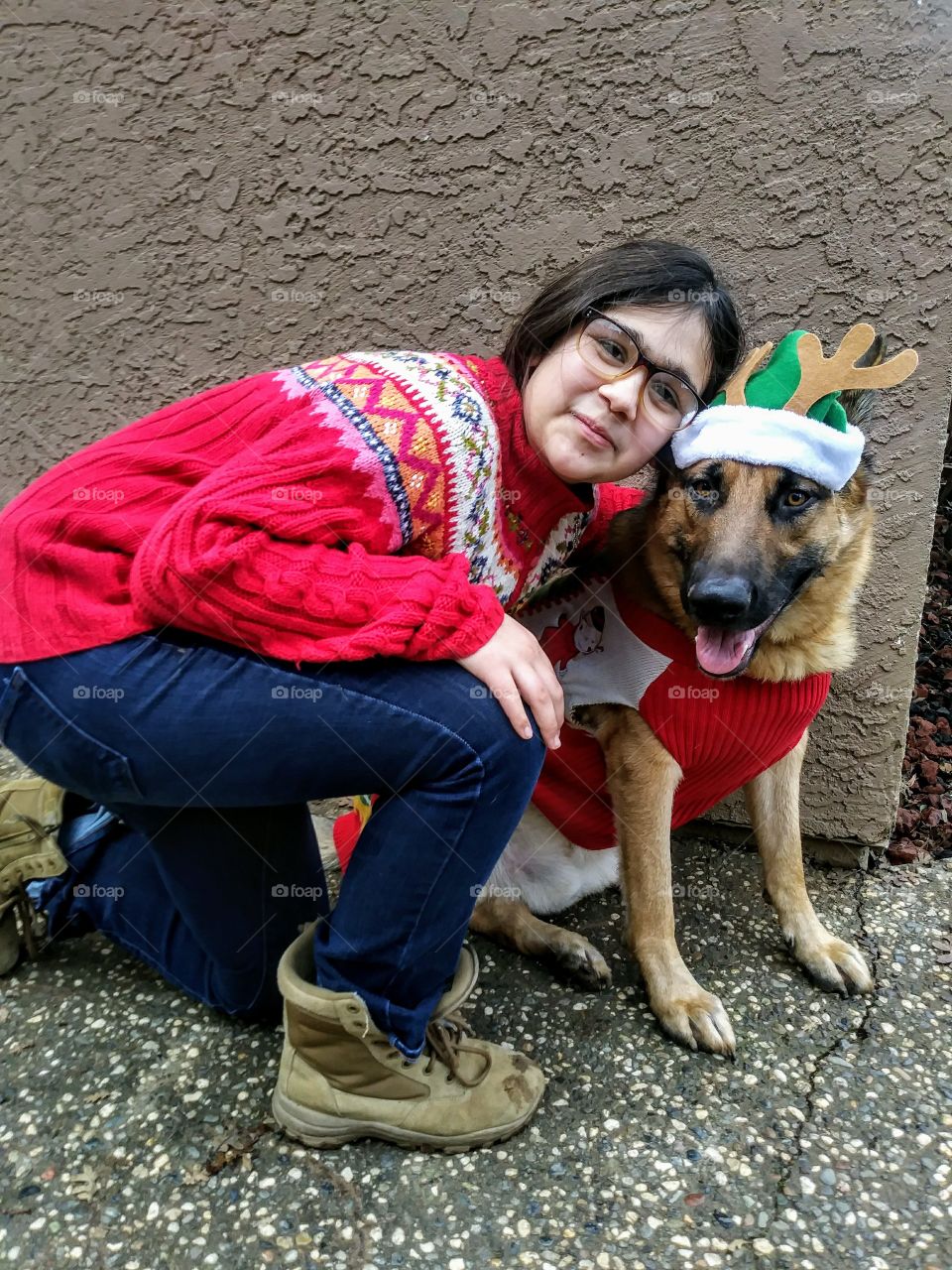 girl poses with german shepherd dog both dressed for christmas. sweaters. dog in hat