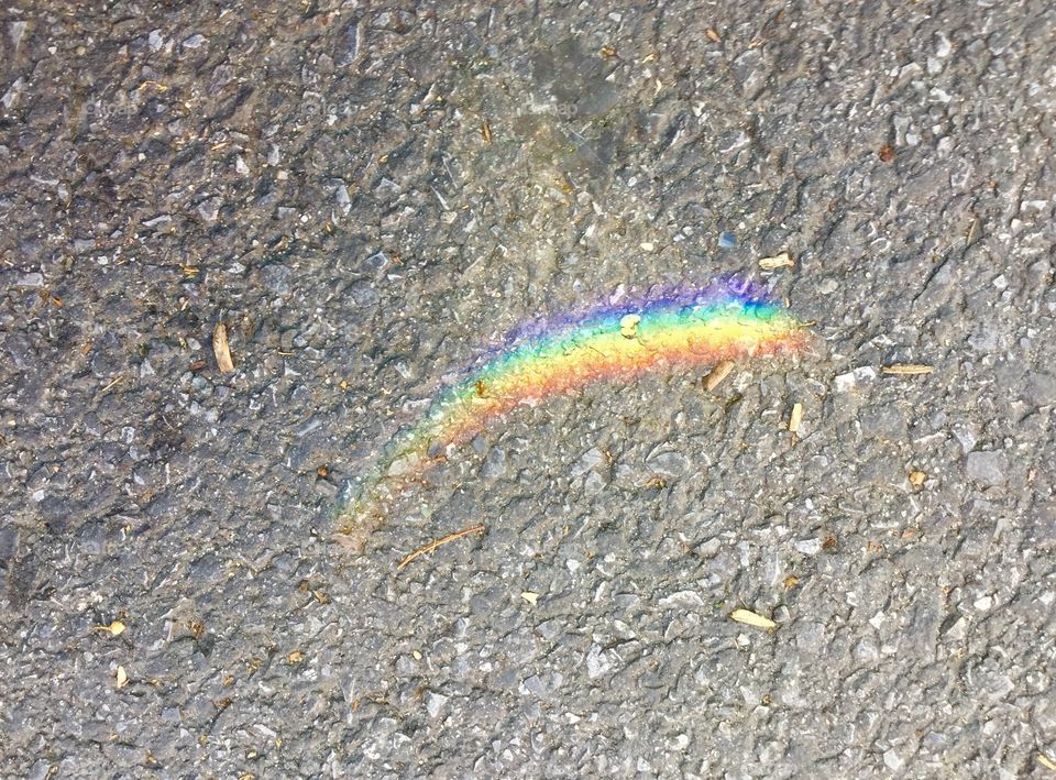 A small, beautiful, gentle, natural rainbow of sunlight shining on a grey cement city street.