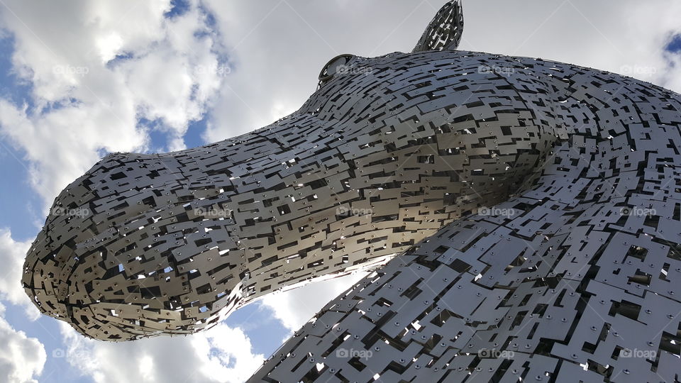 Kelpie art piece in Scotland, shade side to sky with chinks of light and clouds.