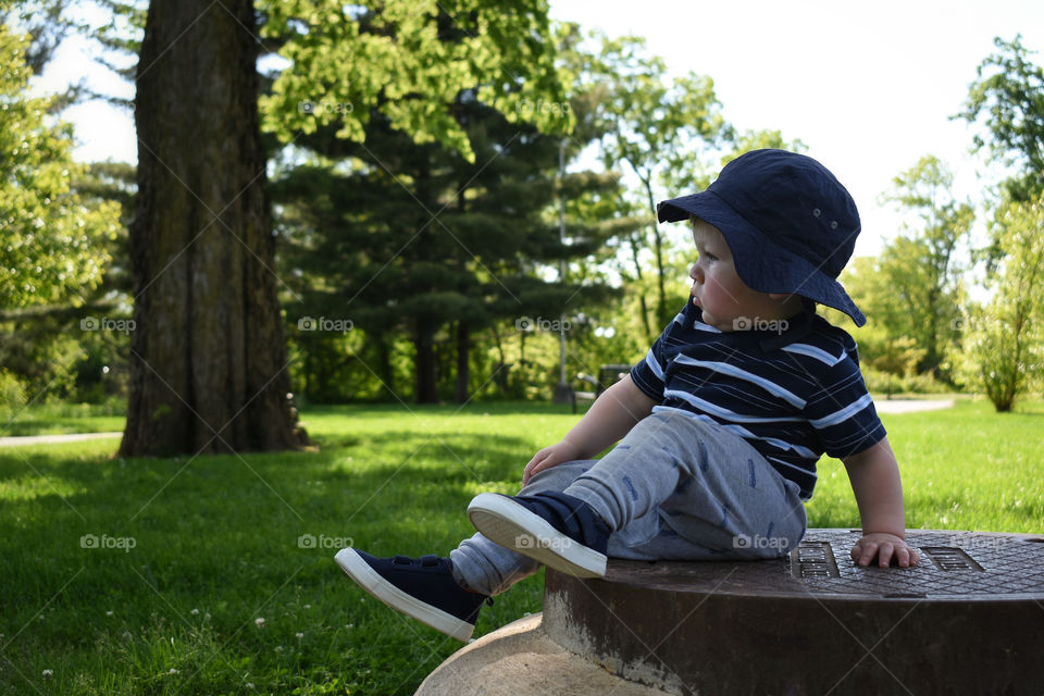 Cute toddler boy sitting on manhole cover in nature park 