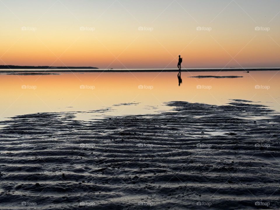 man walking at sunset on the beach in the distance