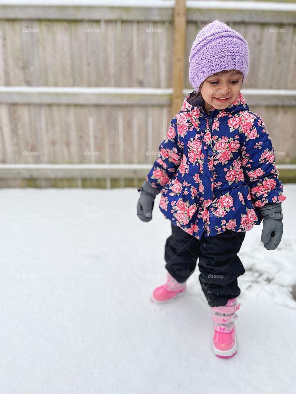 Toddler girl plays in the snow, toddler having fun outside in the wintertime, enjoying the cold weather, kids playing outside, toddler dresses in warm clothes 