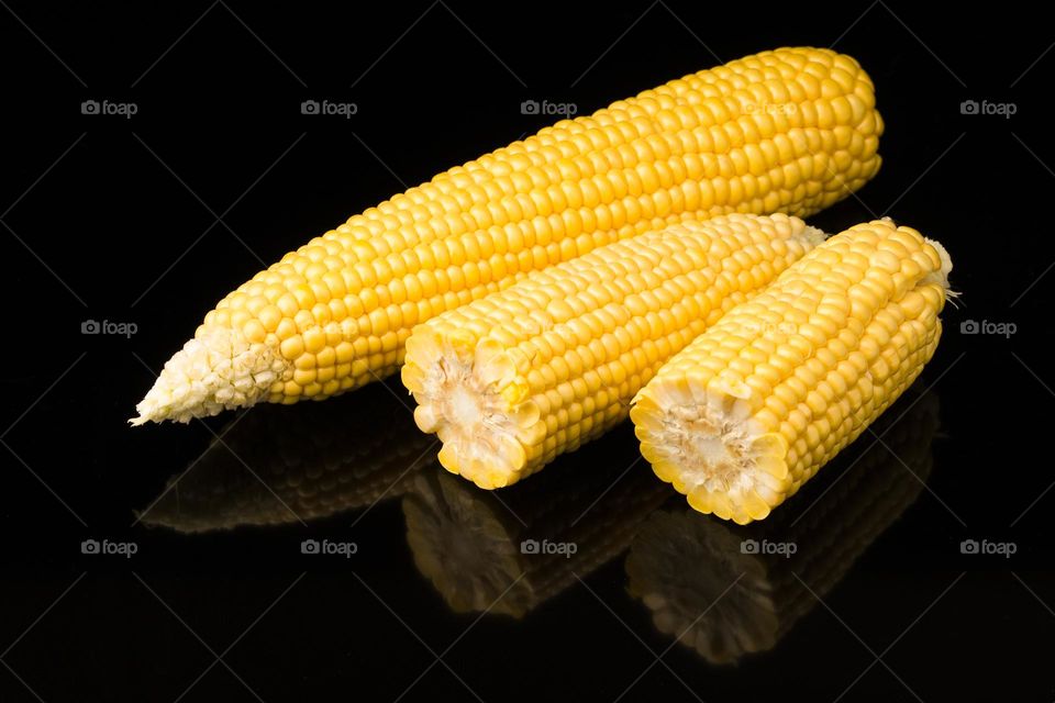 Fresh corn cobs on black background . Close up .