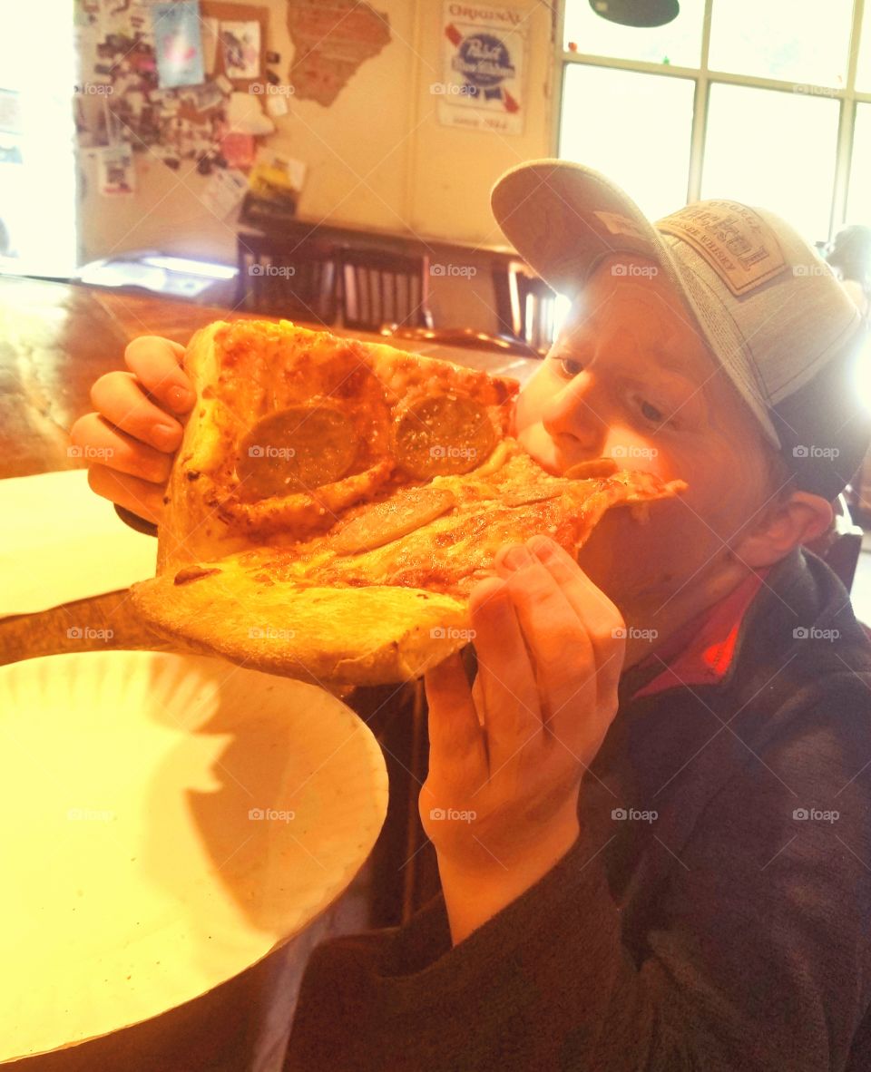 Pizza time as little boy slams a massive slice of cheesy sausage pizza bigger than his face, more napkins please!
