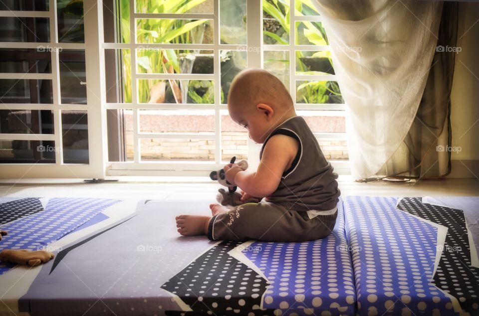A cute baby sits by the window concentrating hard on the task in hand.