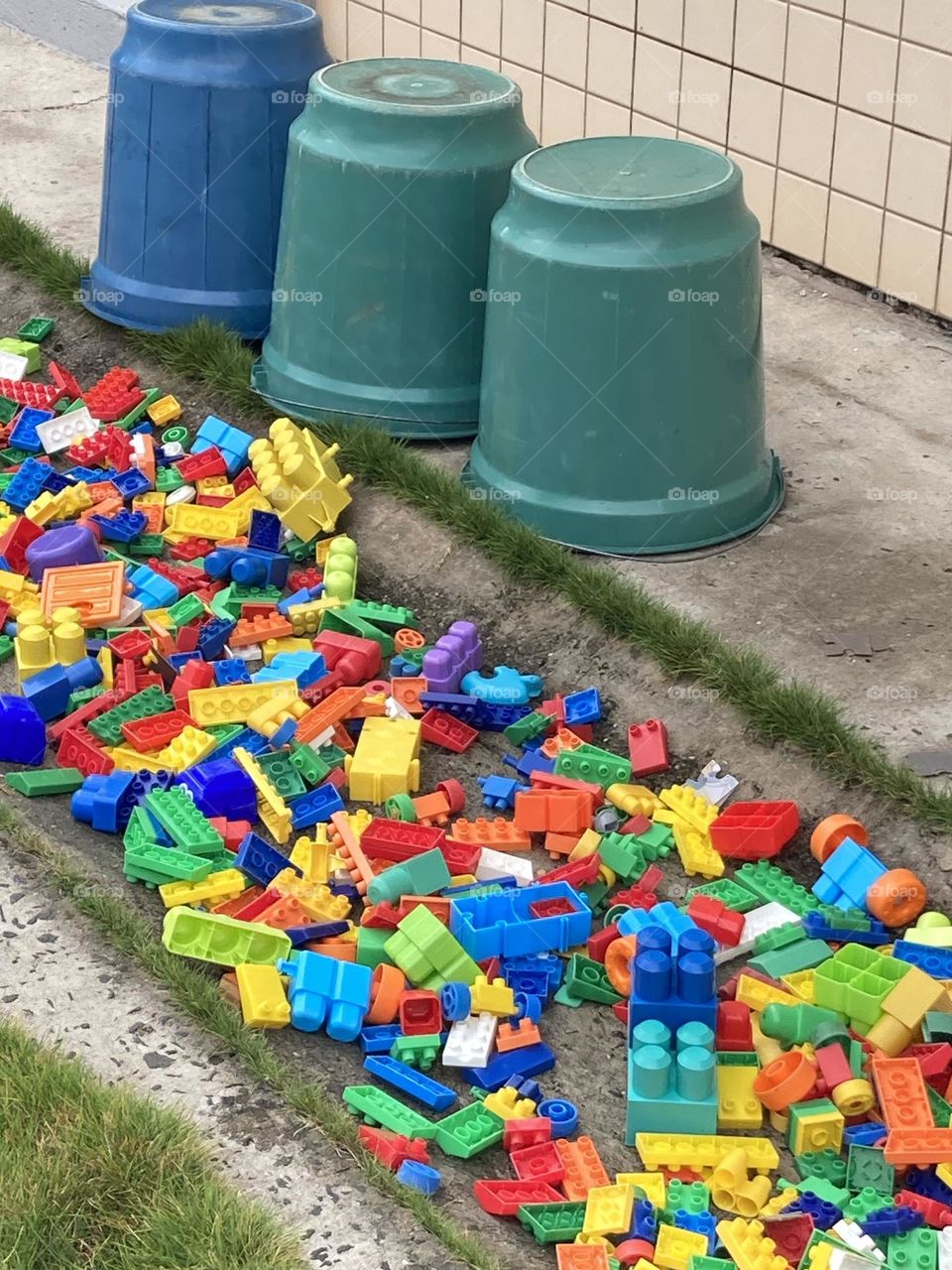Peças de Lego, brinquedo colorido colocadas sobre a calçada para secar pois acabaram de ser lavadas. Baldes coloridos usados na lavagem.
