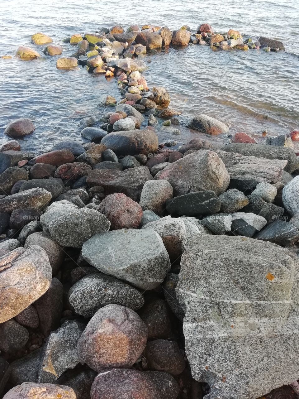Större stenar i det kalla vattnet och sanden bryter av vågorna som kommer från båtarna