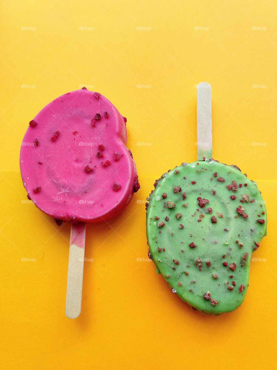 Summer. Time to cool off. On an orange background are two ice creams: red raspberry with raspberry pieces and green kiwi with chocolate pieces. Contrast of colors and taste