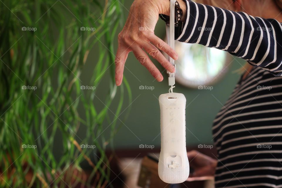 A white controller for a game console hangs with a loop on a woman's hand in living room 